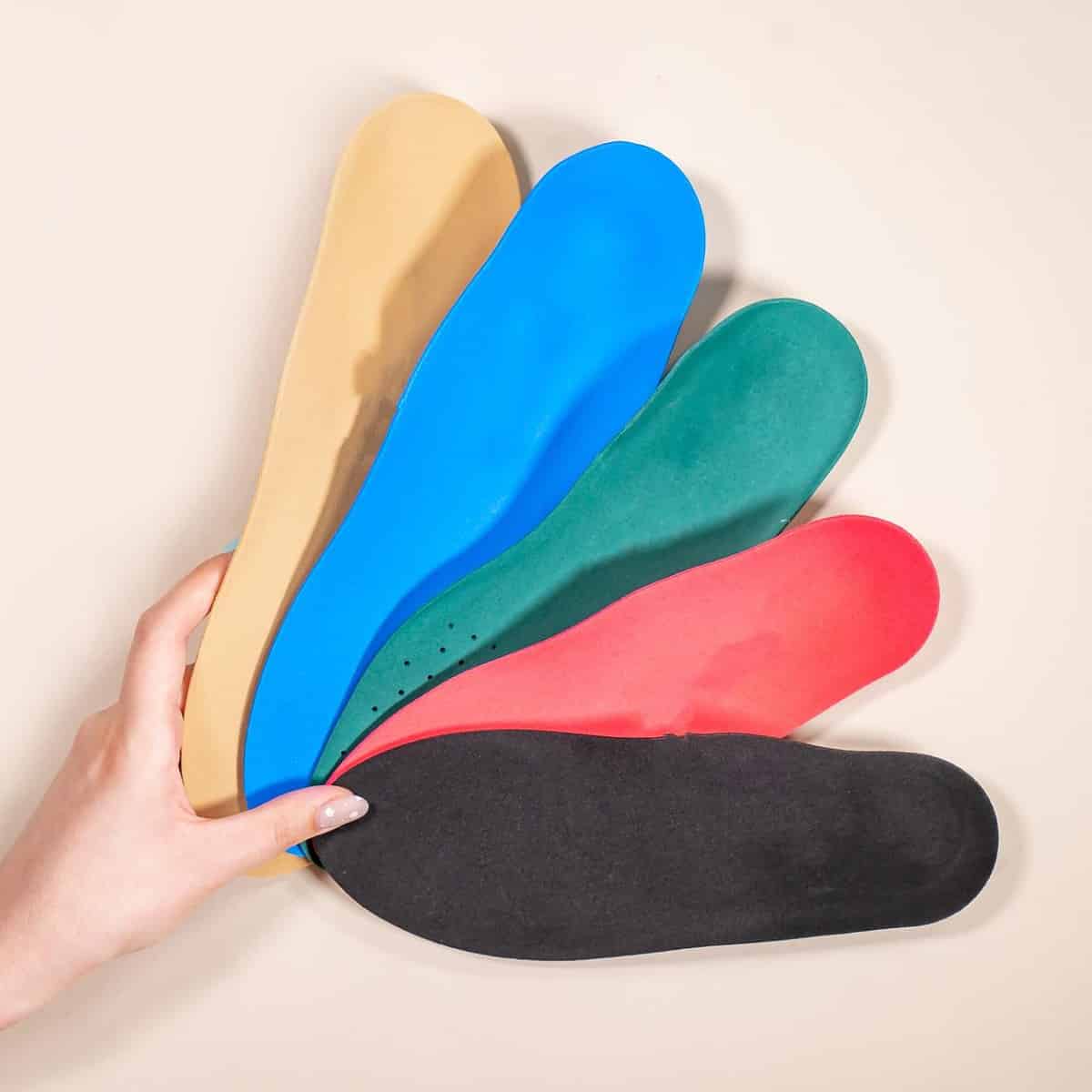 Various foot orthotics being held in front of a cream background